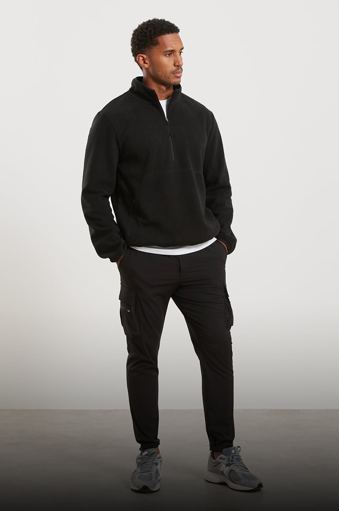 Man wearing a black fleece jacket and cargo pants on a white background
